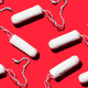 A number of unfurled white tampons are placed artistically against a red background.